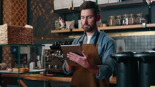Smiling Man Holding Tablet Behind Coffee Shop Counter