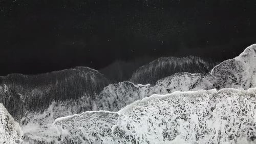 Slow movement of waves on a black sand beach in Iceland. Aerial zenith static shot