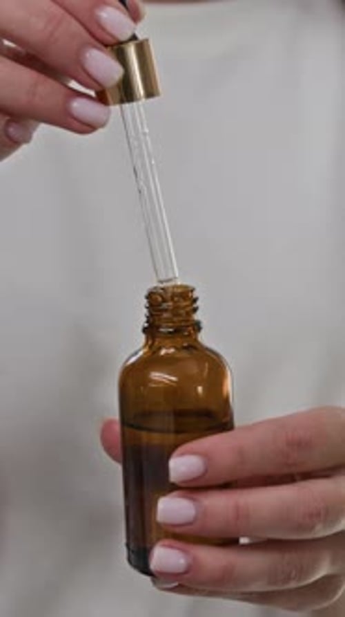 Woman Opening Bottle with Dropper for Beauty Treatment