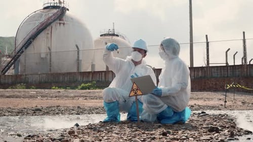 Un biologiste portant une combinaison de protection et un masque prélève un échantillon d'eaux usées provenant de l'industrie
