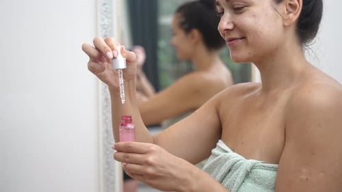 Woman Uses Serum in Bathroom Mirror