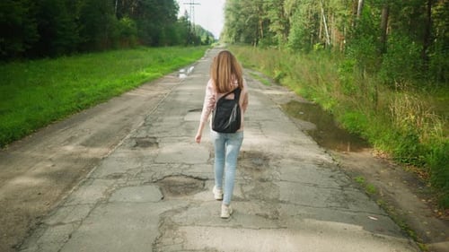 Girl Walking on Worn Tarred Road with Potholes Carrying Bag