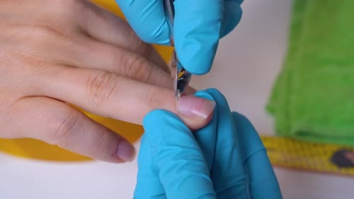 Close-up of the client’s hand and the nail master in processing nails in gloves with a cutter. nail