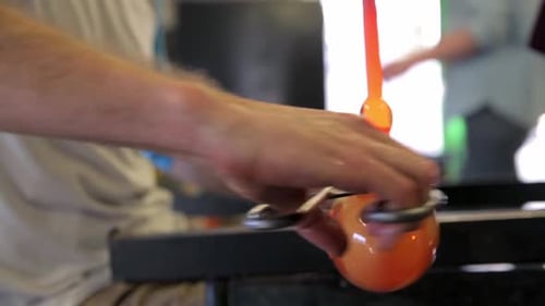 Glassblower shaping molten glass with tools in studio