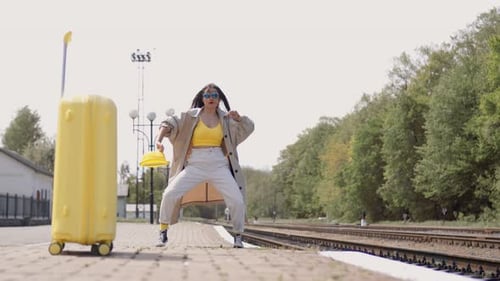 Woman Dancing at Train Station with Yellow Suitcase