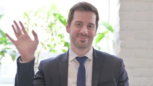 Welcoming Young Businessman Waving Hand for Hello in Office