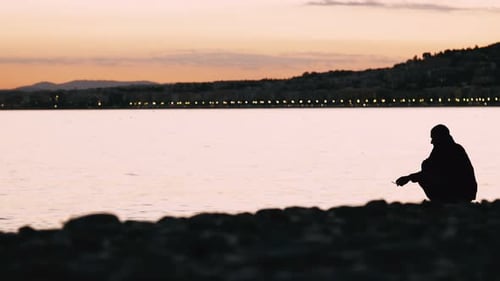 Silhouette eines Mannes, der nach Sonnenuntergang alleine am Strand sitzt Ruhiges Meer Einsam denkende Person