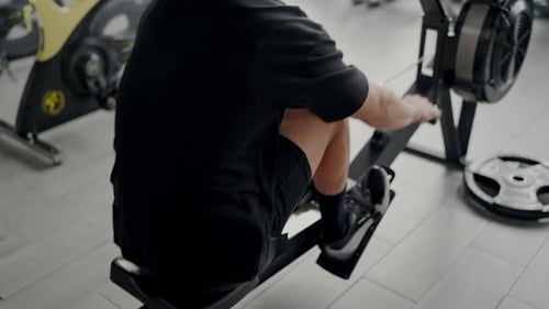 Young Man Exercising on a Rowing Machine in Modern Gym