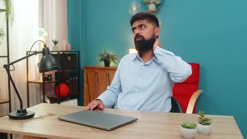 Man works on laptop at desk, massages neck