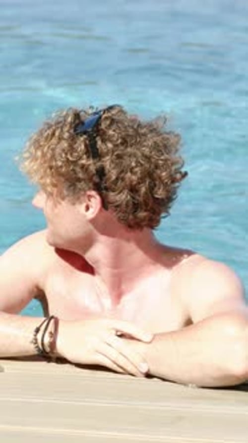 Vertical video: Seeing off frame motion, shirtless man turning head left on dock, shades, bracelets