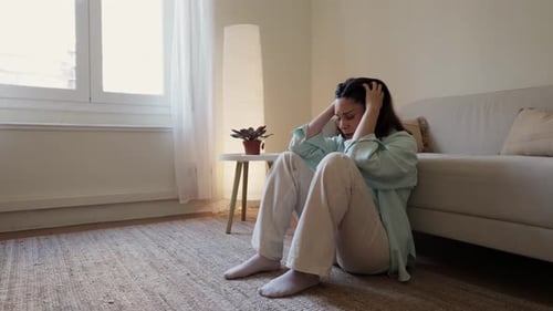 Distressed Woman Sitting on Floor, Looking Out Window