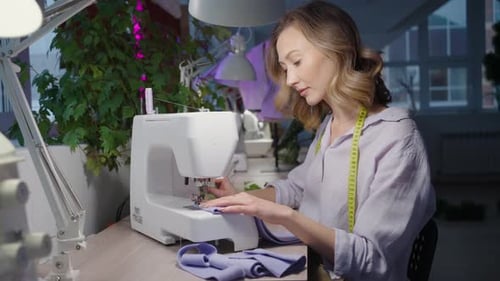 Happy Female Tailor Sewing with a Machine in a Bright Studio