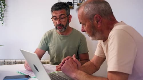 Two Men Discussing Documents and Laptop at Table