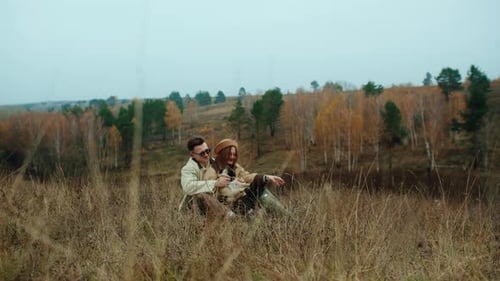 Wide Shot of a Young Couple and Their Pug Dog Sitting and Hugging on a Hill in a Scenic Autumn