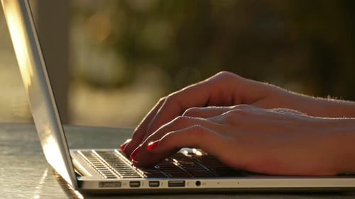 Young woman types on a laptop at sunrise near the beach working outdoors