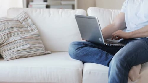 Man typing on laptop computer sitting on sofa at home close up view
