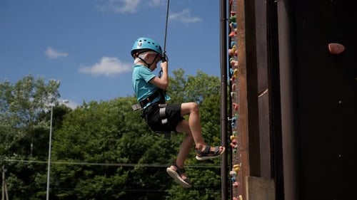 Boy Climbing Rock Climbing Wall with Safety Harness