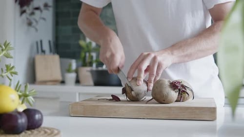 Medium shot of a man cutting fresh beetroot with a knife in a modern kitchen