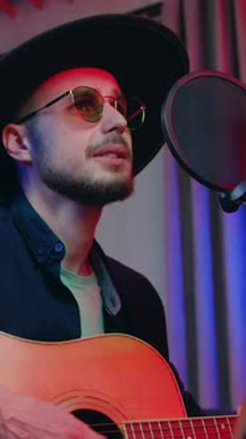 Man Plays Guitar and Sings into Microphone
