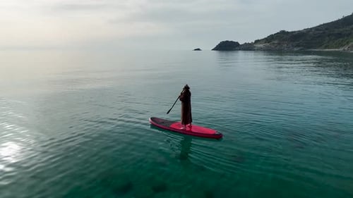 Wide Cinematic Drone Shot Woman Alone on SUP Coat Flowing Paddling Into Infinite Calm Sea with