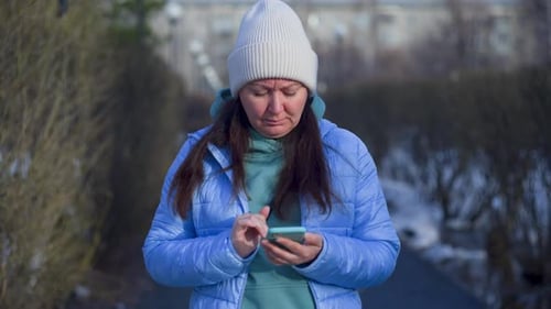 Woman Looking at Smartphone Surfing in Internet Standing on Pathway in Park