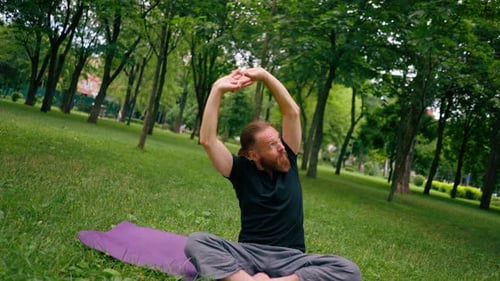 handsome bearded man meditating in the park practicing yoga doing stretching and exercises