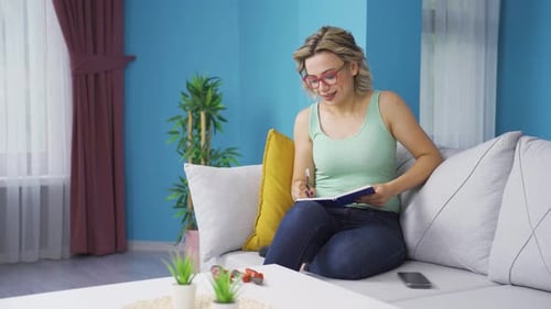 Woman Writes in Notebook on Couch at Home