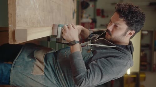 Man Sanding Wooden Plank in Carpentry Workshop