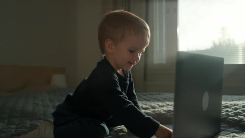 Blond Haired Child Uses Laptop on Bed