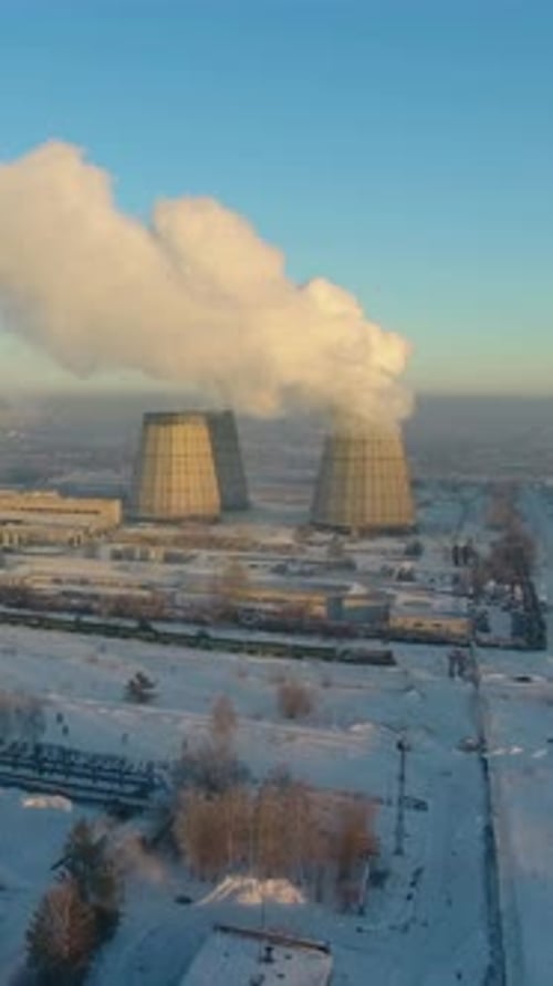 Snowcovered Power Plant Releases Steam Into the Chilly Winter Sky at Sunrise in a Peaceful Landscape