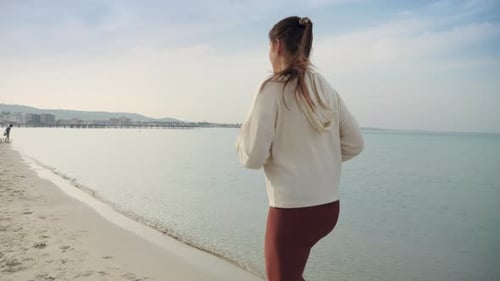 Concept of sports and fitness featuring a young woman jogging on the sandy sea beach