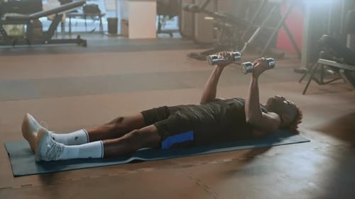 Afroamerikanischer Mann trainiert im Fitnessstudio, liegt auf dem Boden und hebt Hanteln, Powerlifting-Training