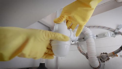 A Plumber in Gloves Collects a Siphon Under the Sink