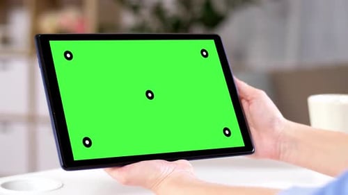 Hands hold a tablet computer with chroma key green screen at home evening