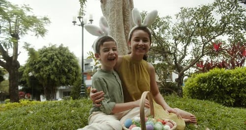 Children with Bunny Ear Headbands on Their Heads are Sitting in a Meadow on Easter Hugging Each