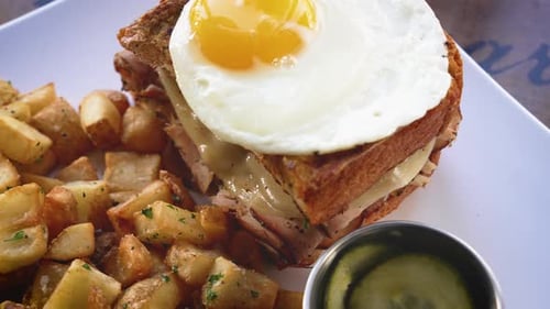 A sunny side up egg topping a breakfast sandwich with home fries, slider close up 4K