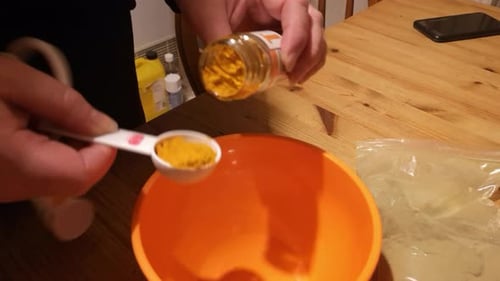 Female measuring Moringa and turmeric powder herbal remedy supplement in orange bowl