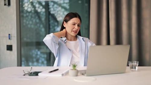 Woman at desk rubbing sore neck, shoulder pain