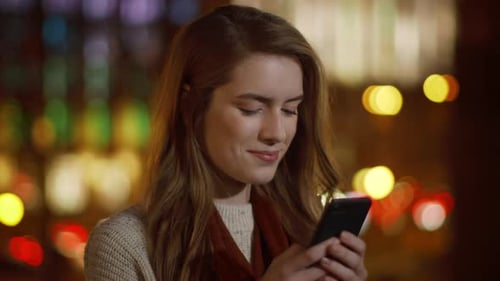Smiling woman uses phone at night, city lights
