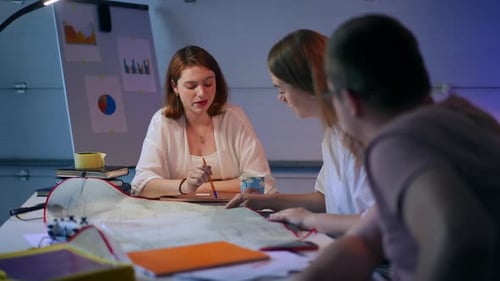 Jeune femme rousse séduisante parlant avec un collègue assis à table avec un plan architectural
