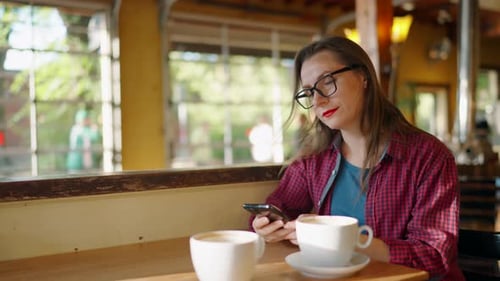 Woman is Using Smartphone and Drinking Coffee in the Cafe