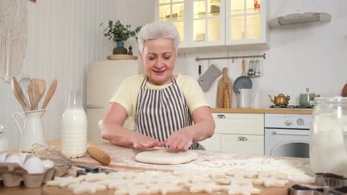 Gray Haired Woman Flattens Dough in Bright Kitchen