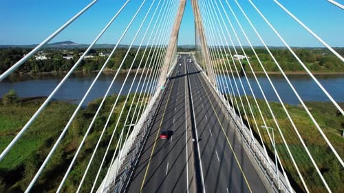 suspension bridge drone moving along bridge between cables with traffic flowing below over river in