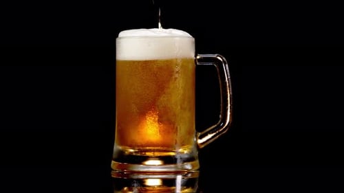 Pouring Lager Beer Into A Beer Mug With Froth In Black Background - studio shot