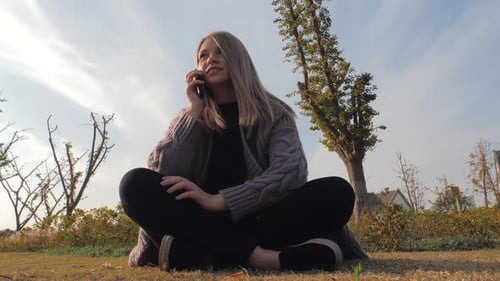 Young Attractive Blonde Girl Sitting Outdoors in Park Using Phone