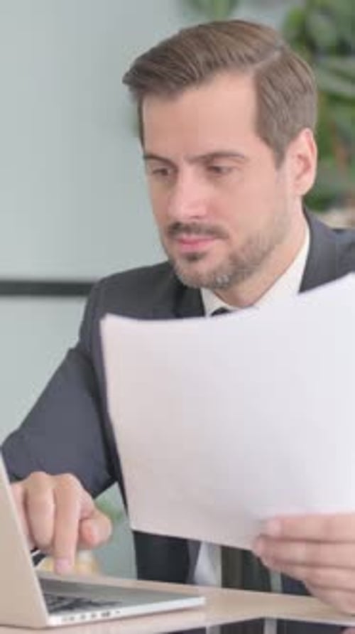 Focused Man Reviews Documents While Typing on Laptop