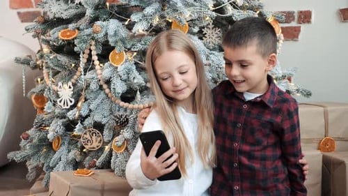 Children Using Phone in Front of Christmas Tree