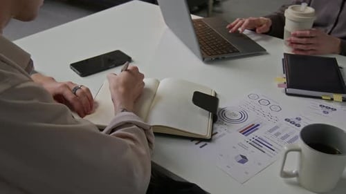 Unbekannte Büroangestellte, die in ein Notizbuch schreiben und den Laptop benutzen