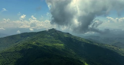 Flying trough white fluffy clouds above green mountain peaks. Beautiful summer sunny day on the high