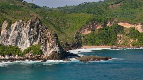 Aerial rocky green island cliff with waves and hidden tropical beach cove